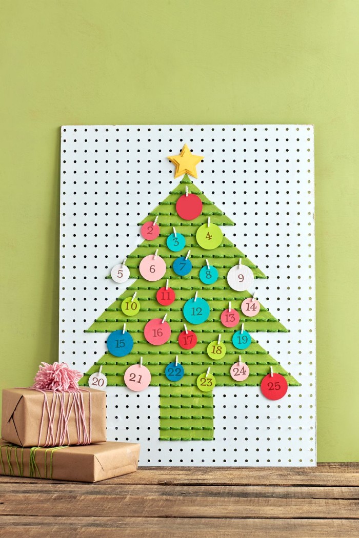 board with multiple holes, featuring a christmas tree shape, painted in green, and decorated with green thread, christmas countdown calendar, round small labels, in different colors and sizes, attached with miniature pegs