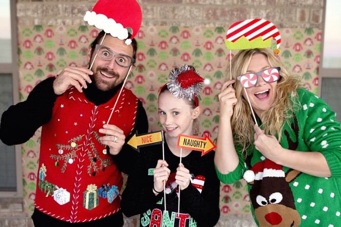 family with a mom, dad and a daughter, all dressed in different tacky festive jumpers, ugliest christmas sweater, red with an xmas tree, black with a festive message, green with white polka dots, and a cartoon deer's head