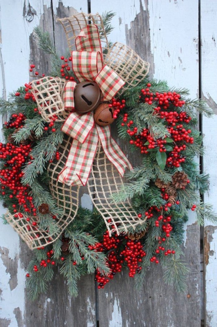 bells in rusty orange and borwn, decorating a wreath, made from pine branches, adorned with multiple red berries, and large bows, made of burlap, and a checkered fabric