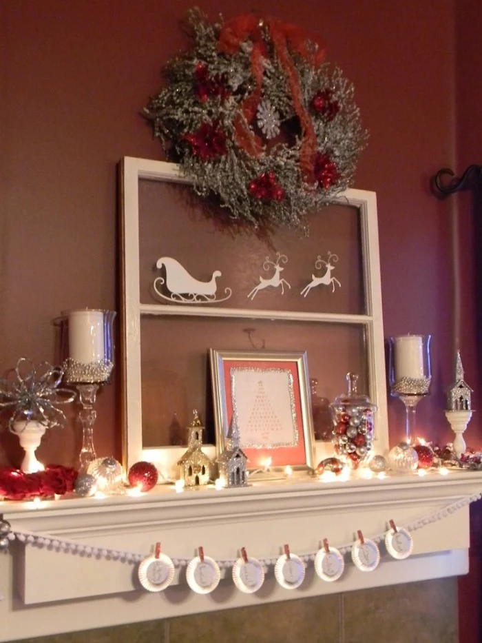 brown wall near a white mantel, decorated with a silver and red wreath, a frame with santa's sleigh and two reindeer, candles and more, diy fireplace mantel ideas