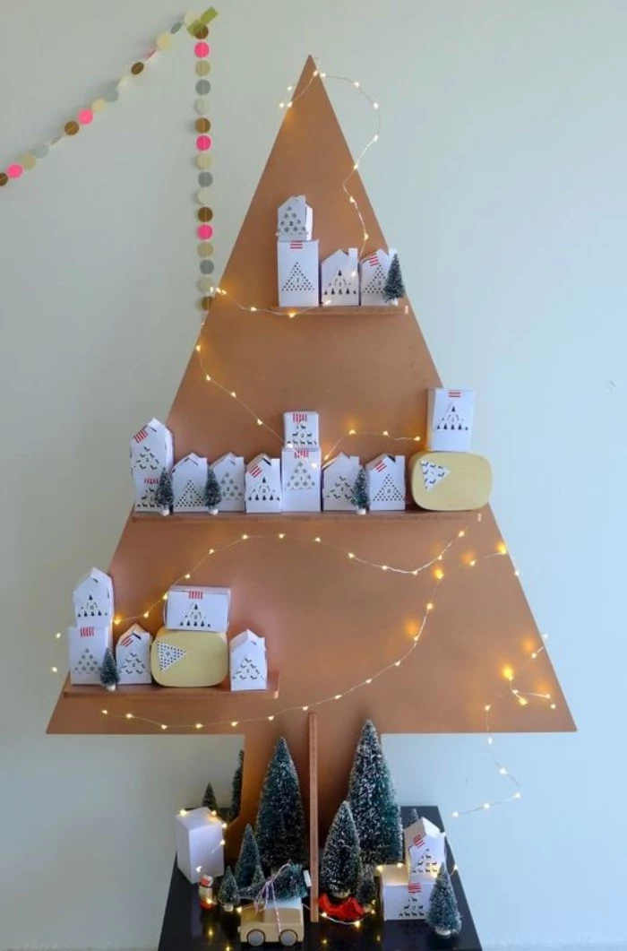 triangular christmas tree decoration, made from beige cardboard, with three shelves, containing small white boxes, advent calendar ideas, small lit string lights, and various decorations