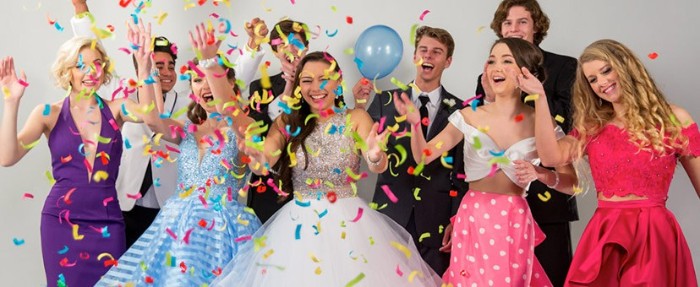 multicolored confetti and a blue balloon, next to a group of celebrating teenagers, wearing prom dresses, and formal suits