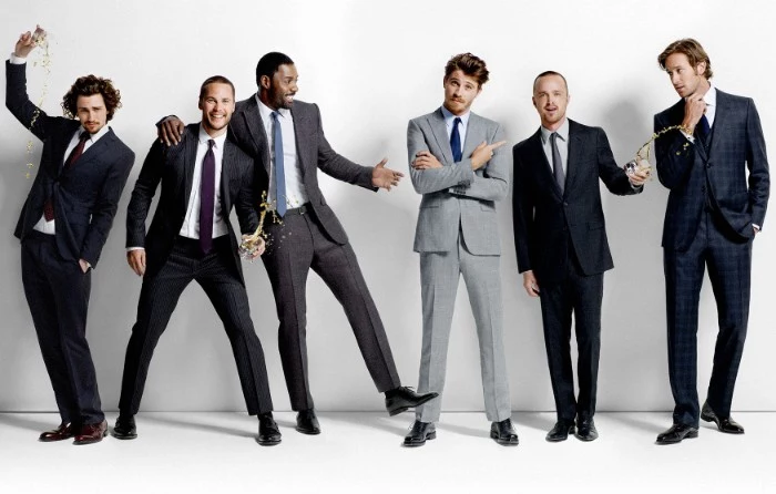 six men dressed in smart suits, in light grey, dark grey and navy blue, cocktail attire for men, smiling and posing for a photo