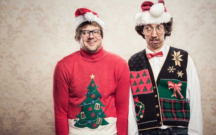 two men wearing festive, multicolored sweater and vest, and stanta hats in red and white, ugly christmas sweater ideas, xmas trees and bows, snowflakes and a wreath