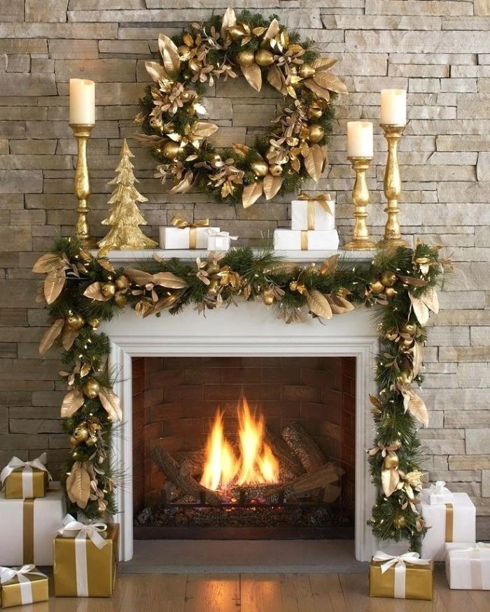 gold leaves decorating a green wreath, made from faux pine leaves, and a similar green garland, draped over the mantelpiece of a burning fireplace, christmas mantel ideas, in green and gold