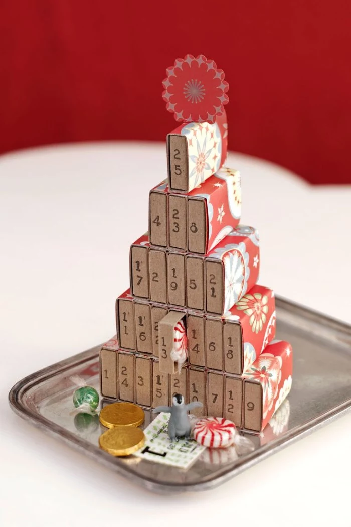 diy advent calendar, made from several matchboxes, decorated with colorful patterned paper, and stacked to form a christmas tree, various candies and a small toy