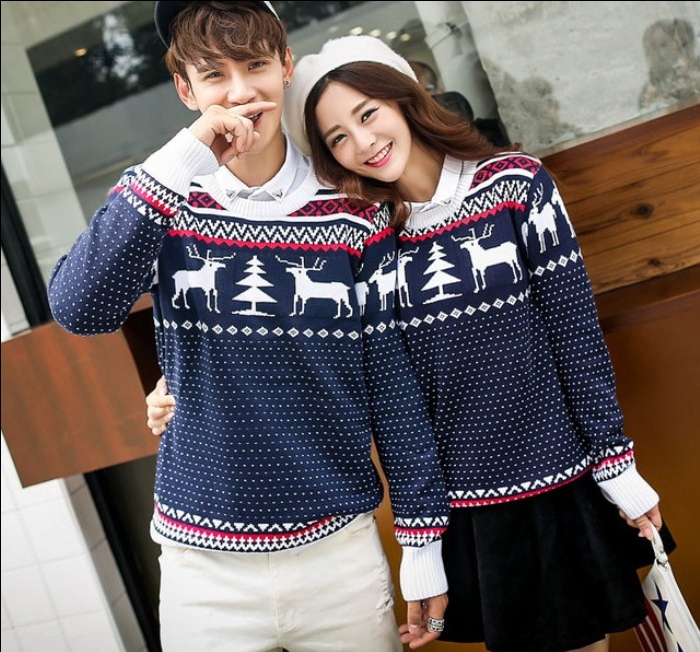 identical navy blue sweaters, with white and red fair isle motifs, featuring deer and christmas trees, worn by a young smiling couple, ugly sweater party