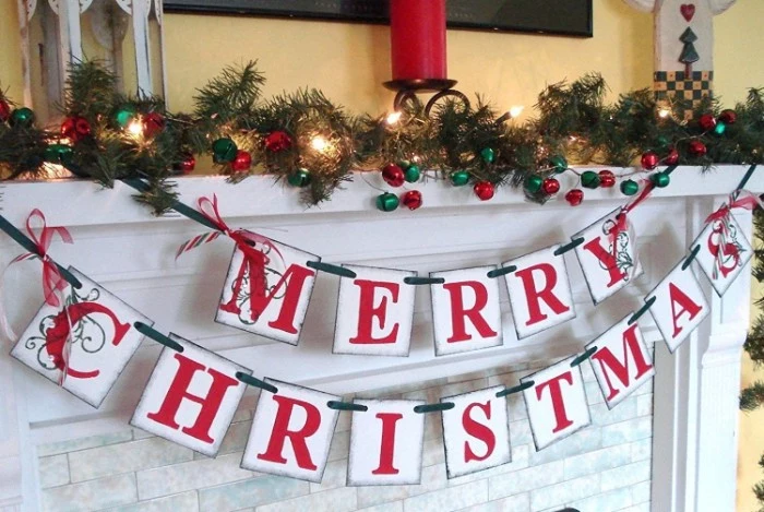 banners with the words, merry christmas written in red, hanging from a white mantelpiece, images of christmas, pine garland and glowing fairy lights