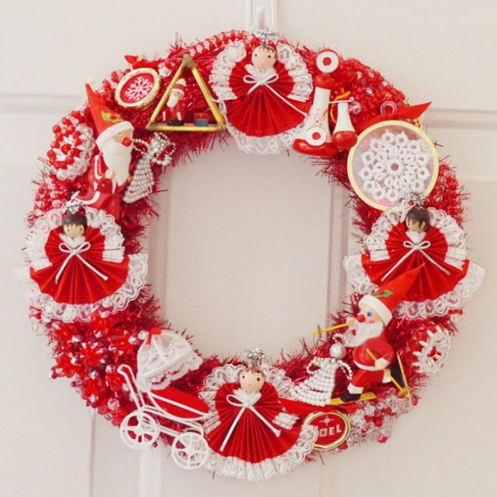 dolls and small decorations, in red and white, on a diy wreath, made from a red fuzzy garland, and hung on a white door