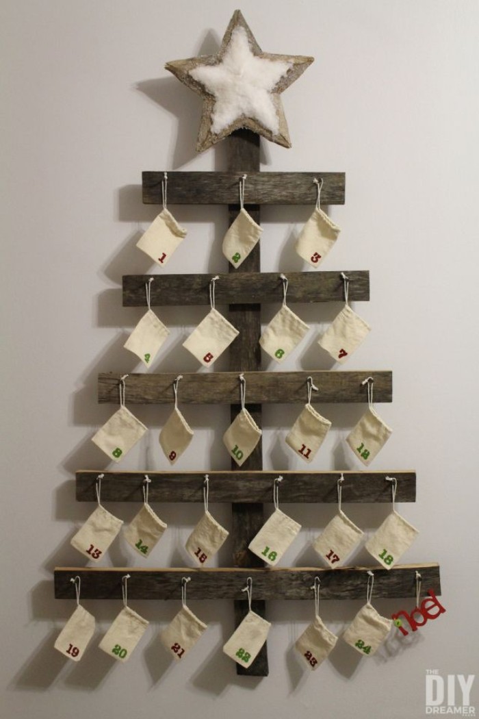 pieces of wood, attached together to form a minimalistic christmas tree, with a star on top, the three is decorated with 24 small, numbered pale cream drawstring bags, hanging on nails