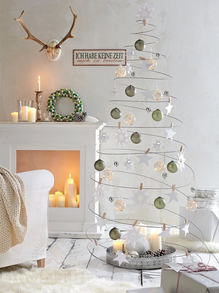 xmas tree made from wire, twisted into an upward spiral, and decorated with white, silver and gold baubles, small wreath and several candles, on a diy fireplace mantel nearby