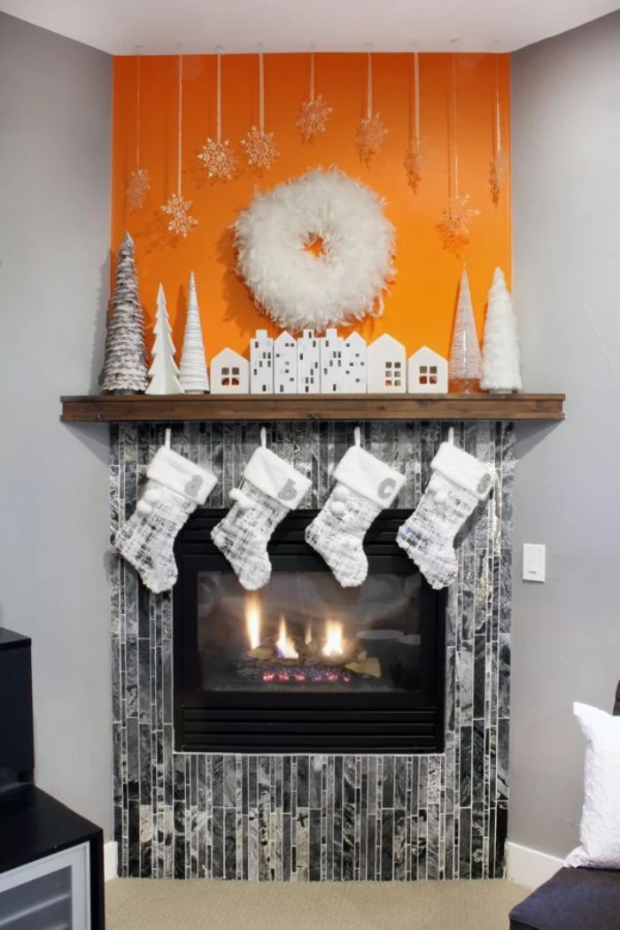 orange and grey walls, in a room with white, and silver chirstmas decor, featuring small house and xmas tree figurines, and four stockings, on a diy fireplace mantel