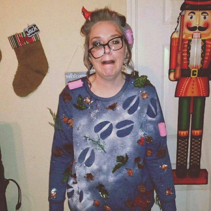 humoros christma costume idea, blue jumper covered in faux deer hoof prints, fake leaves and small branches, worn by a woman, with askewed glasses, girls ugly christmas sweater, run over by rudolph