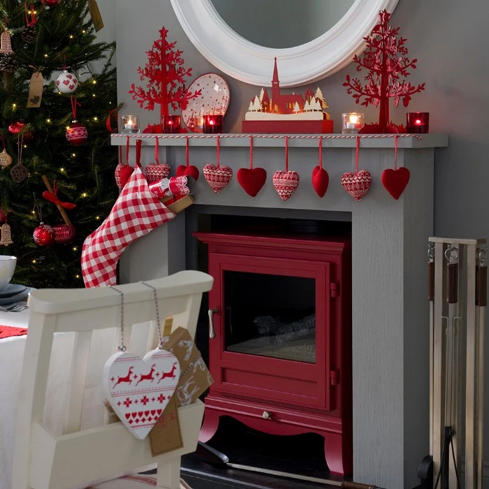 christmas fireplace, decorated with white and red, stuffed heart ornaments, hanging from a red and white rope, small candles and red christmas tree figurines