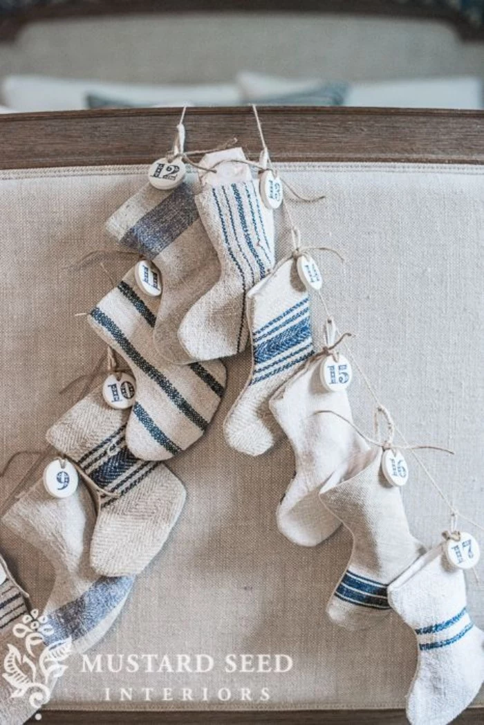 burlap small decorative stockings, in pale beige, with inky blue stripes, hanging on a piece of rope, each stocking has a small, round white tag, with a number, from 1 to 24