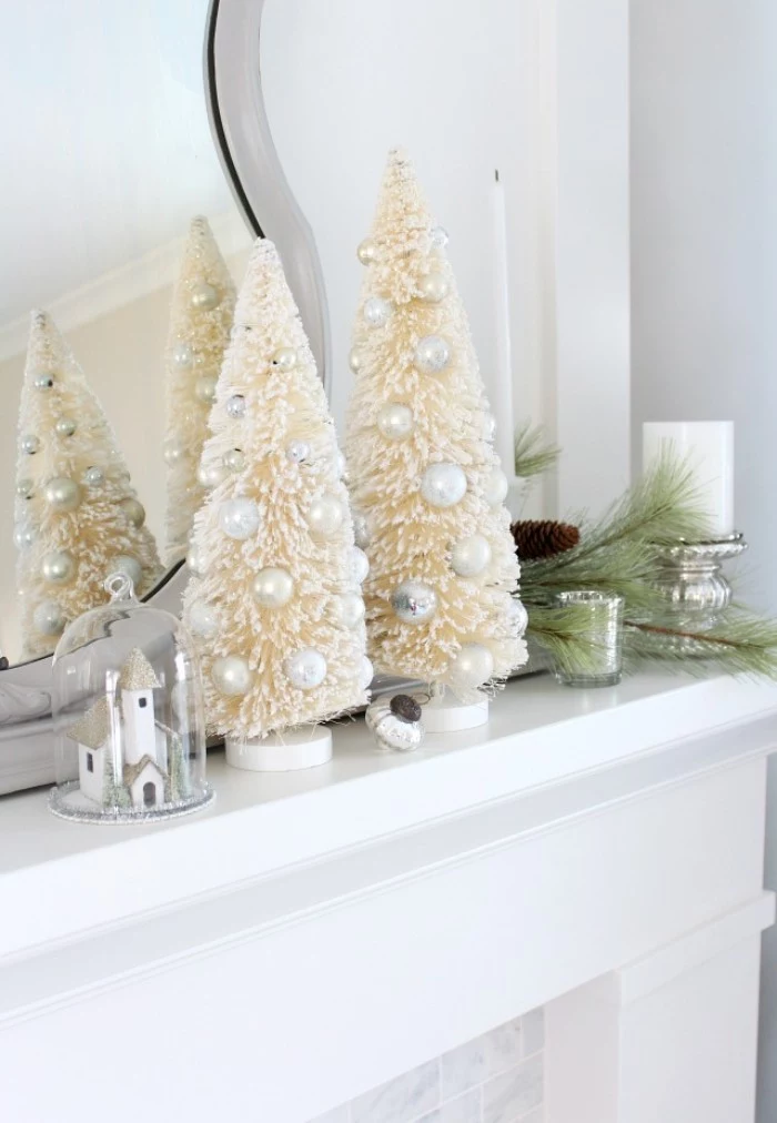 what to put on your christmas fireplace, two cream christmas tree figurines, adorned with white faux pearls, near a small church decoration, under a glass dome
