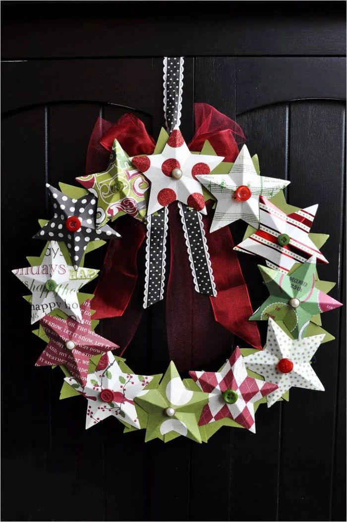 stars made from colorful patterned paper, stuck onto a wreath, decorated with pins and buttons, a sheer red bow, and a black and white ribbon, christmas wreath images, hanging on a black door