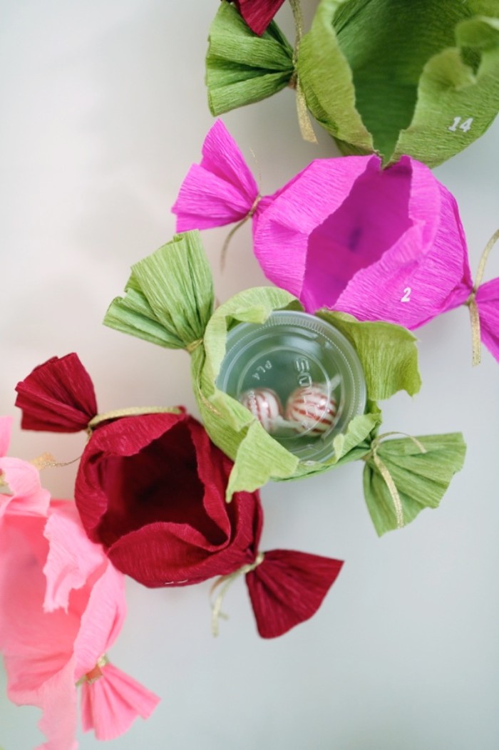 several ripped present wrappers, shaped like candy, in different colors, four are empty, and one contains a clear, plastic round box, with two peppermint candies, christmas advent calendar suggestion