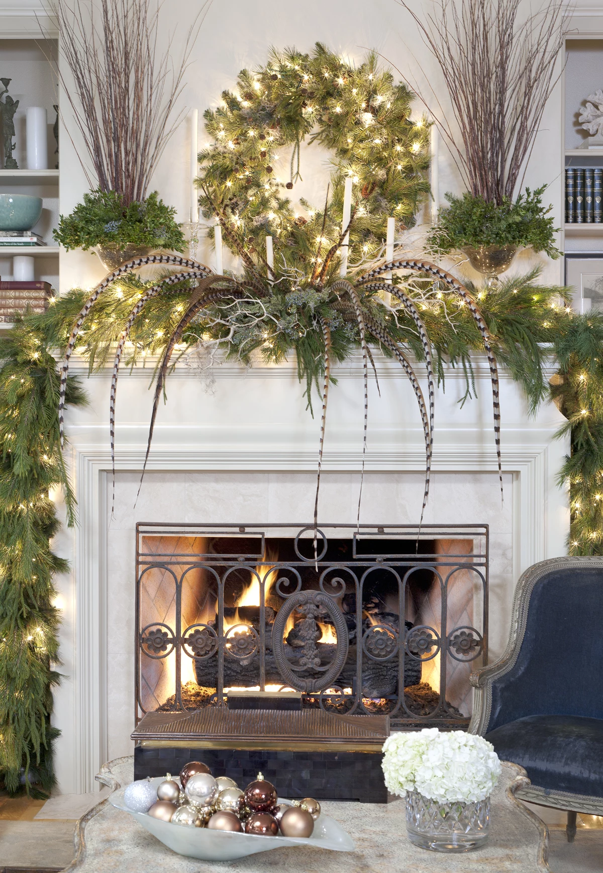 christmas mantel ideas, white lit fireplace, decorated with green pine garlands, a classic pine wreath, pheasant feathers and glowing string lights