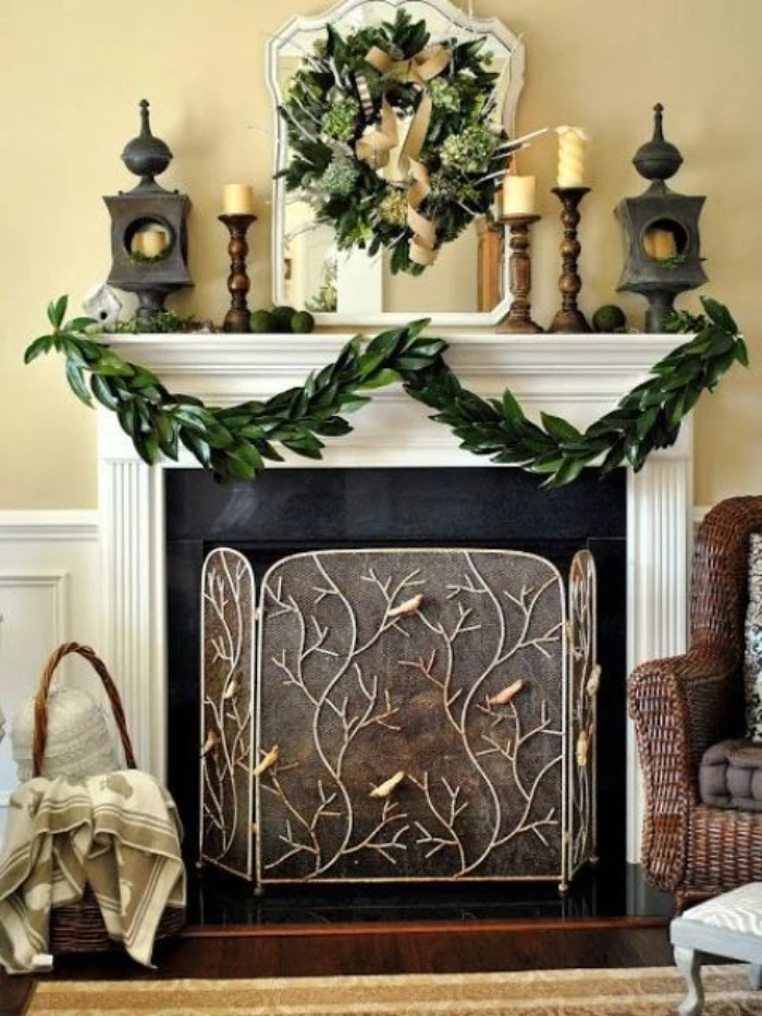 ornate fireplace grate, with branches and birds motif, placed in front of a black and white fireplace, decorated with a garland, made from green leaves