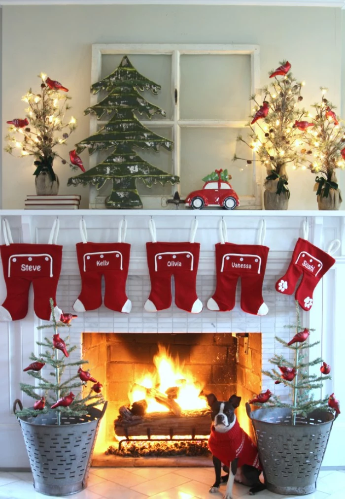 five red and white rompers, hanging on a white mantelpiece, decorated with several small christmas tree ornaments, and a small red car, fireplace decor