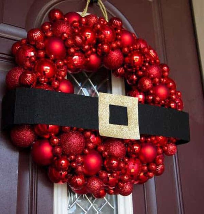 belt made from black cardboard, with a buckle covered in gold glitter, decorating a diy wreath, made fromred baubles stuck together, santa clause-themed decoration