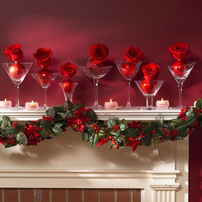 cocktail glasses with different designs, placed on a white mantel, near burning tea lights, christmas mantel ideas, each glass contains a red rose, attached to a red christmas bauble