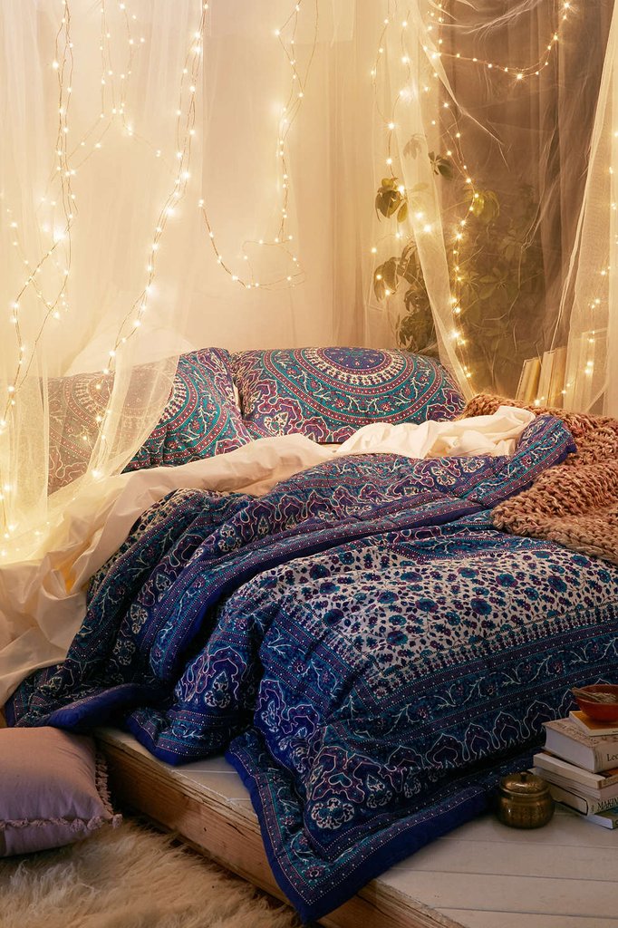 glowing fairy lights, on a sheer white baldachin, over a double bed, with blue and white, boho-style bedding