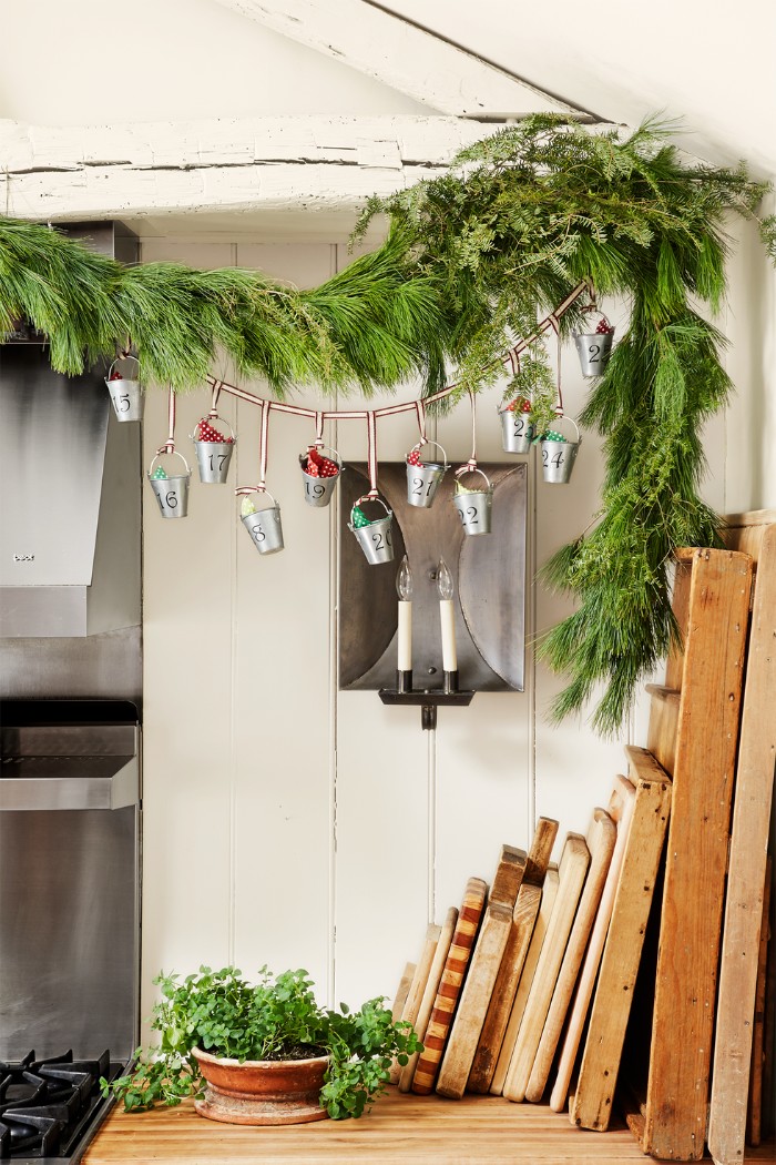 advent calendar ideas, silver colored miniature, numbered metallic buckets, filled with small gifts, hanging near a garland, of pine and fir branches