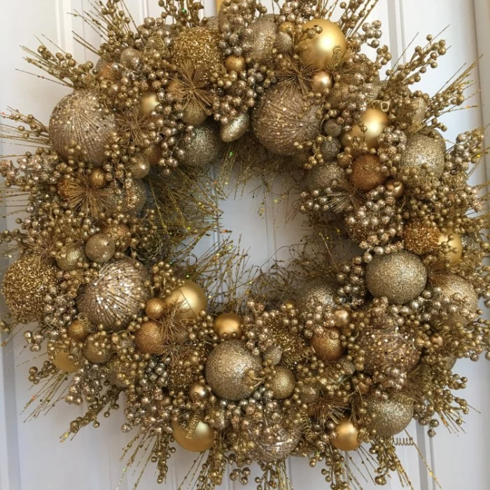 gold wreath made from round, christmas ornaments in different sizes, and thin faux branches, with multiple tiny berries, all in gold hues