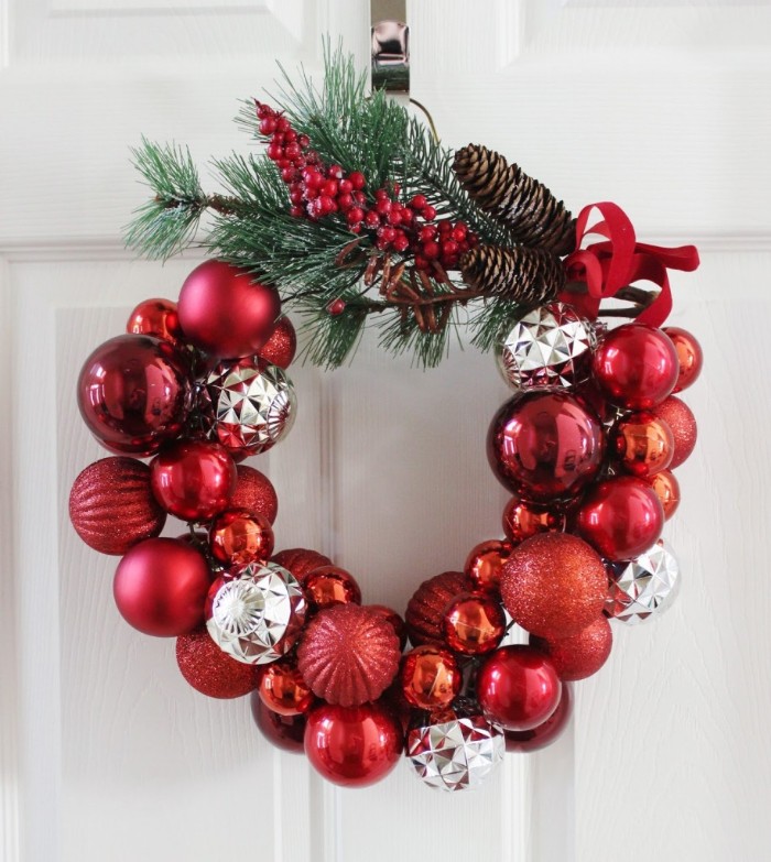 red and silver christmas tree baubles, stuck together to form awreath, decorated with pine branches, red berries and pine cones, christmas wreath images, on a white door