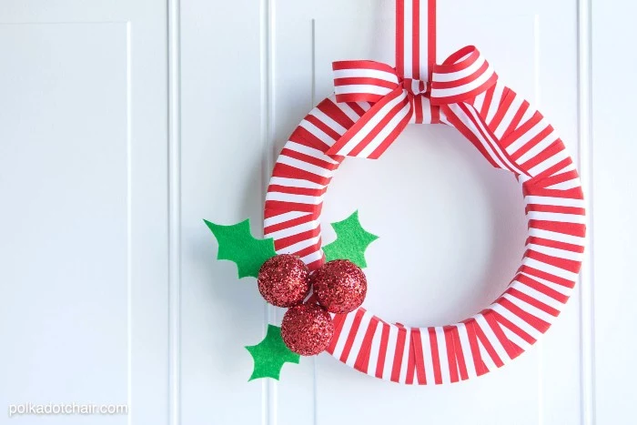 striped red and white wreath, decorated with three baubles, covered in red glitter, three holly leaves, made of green felt, and a large striped bow, christmas wreath