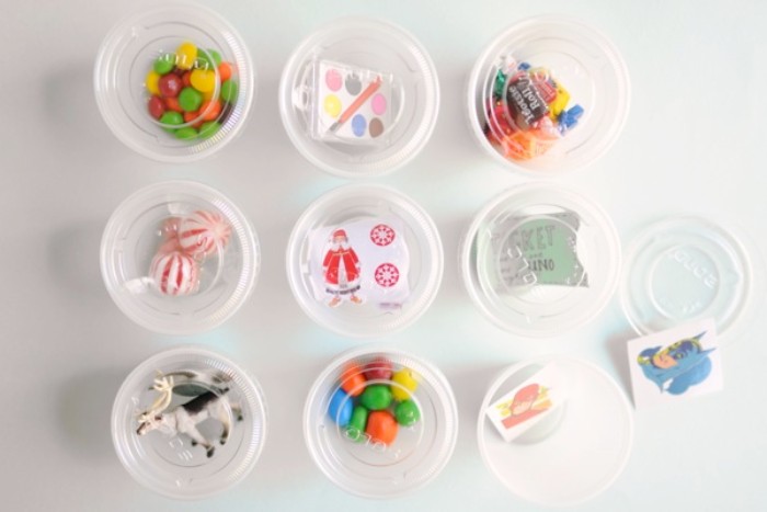 nine small round, plastic boxes with transparent lids, or candy containers, filled with different sweets, and small toys, advent calendar made at home