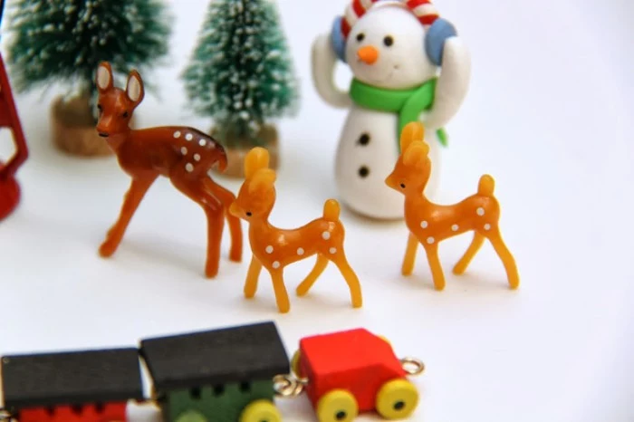 deer figurines made of brown plastic, near a snowman toy, several tiny christmas trees, and a miniature wooden train, advent calendar stuffings 