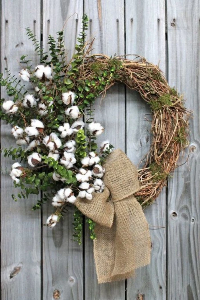 cotton seed pods on branches, with small green leaves, decorating a rustic wreath, made from thin, dried twisted branches, tied with a burlap bow
