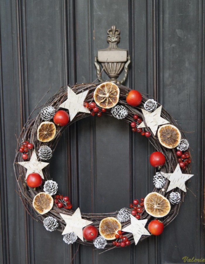 birch bark star shapes, decorating a diy christmas wreath, made from thin dried branches, and adorned with small pinecones, covered in silver paint, dried orange slices, and faux red berries in different sizes