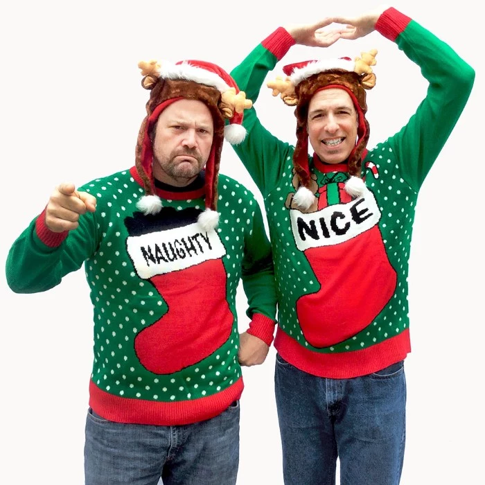green jumpers with white polka dots, and red and white christmas stockings, one saying naughty and the other nice, ugly christmas sweater ideas, on two men, wearing hats with small fabric deer antlers