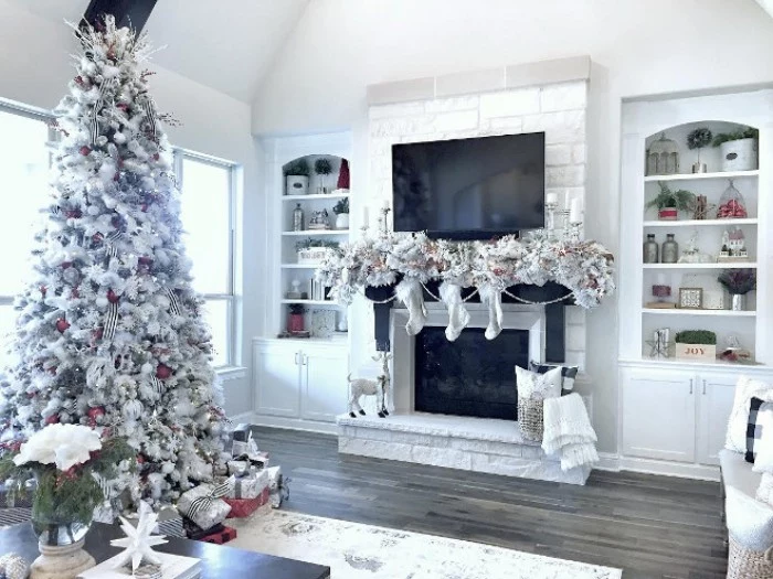 white and silver christmas decorations, draped over a black and white fireplace, christmas mantel ideas, a tall faux christmas tree in white standing nearby