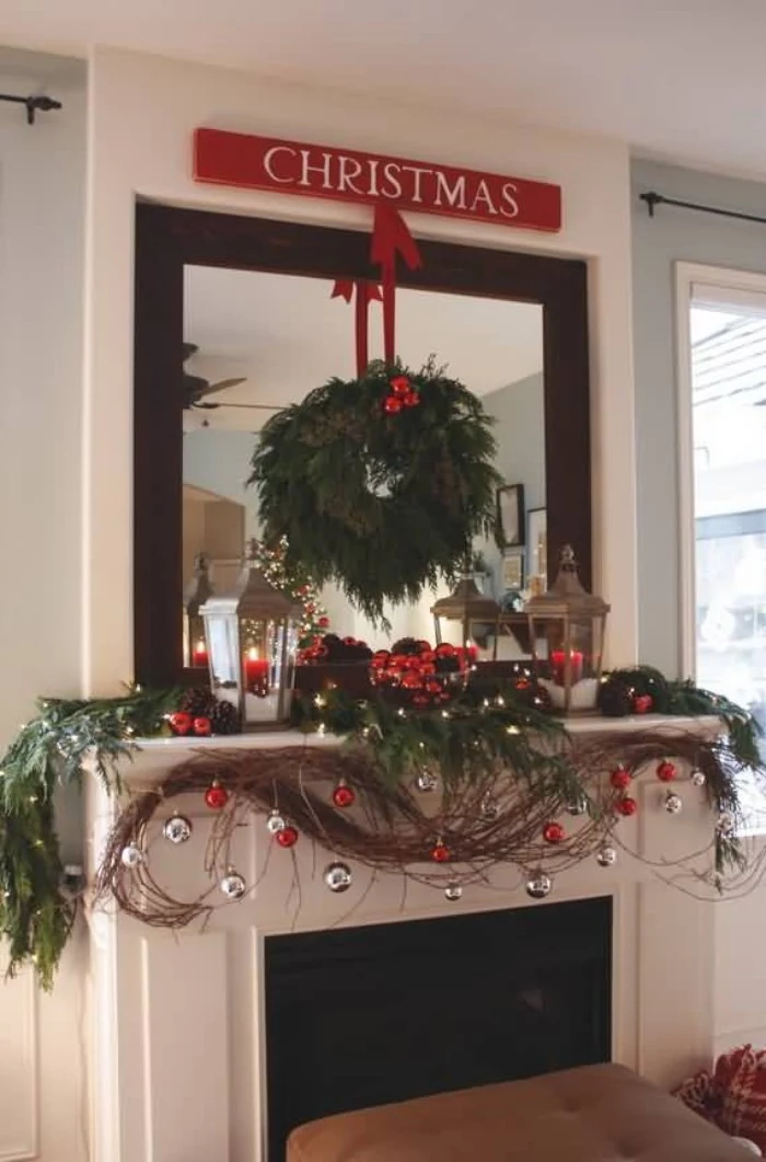 baubles in silver and red, hanging from a garland, made from brown, and green artificial branches, draped over a white fireplace mantel, green pine wreath, with red details, hanging on the large mirror overhead