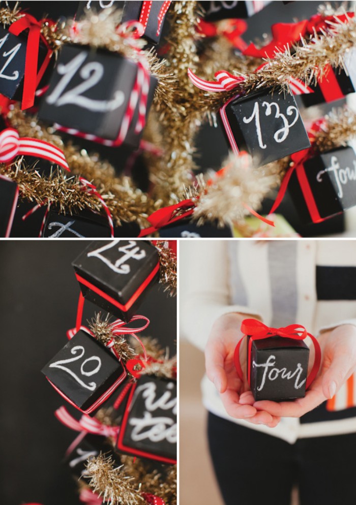 close up of a gold, faux christmas tree, decorated with small, black cube-shaped boxes, decorated with numbers written in white chalk, and red ribbon tied in bows, diy advent calendar, hand holding one of the boxes