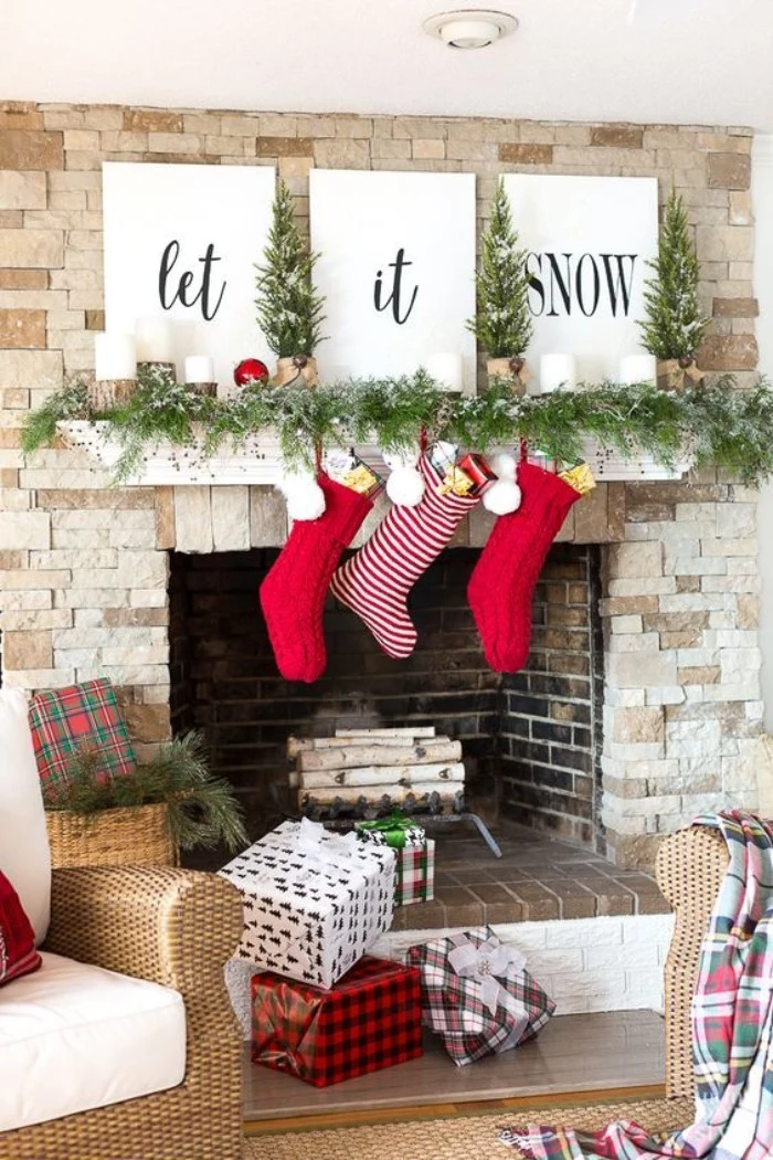 fireplace mantel decor, featuring three white canvases, with the words, let it snow, written in black cursive, a green garland, and three red and white stockings