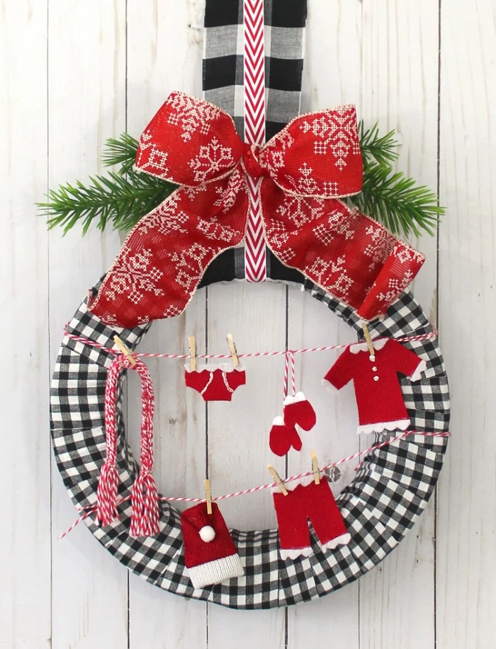 washing lines made from striped, red and white yarn, featuring small red and white clothes, hanging on miniature pegs, christmas wreath ideas, on a wreath covered in black and white checkered fabric, and decorated with a large red and white bow, and pine leaves 