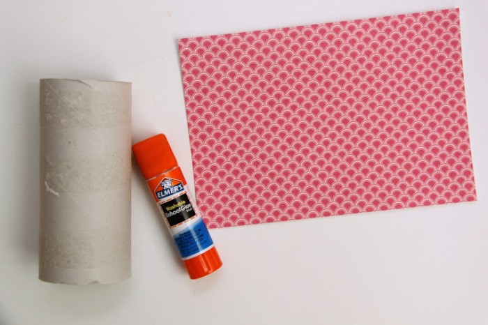 what you will need, to make a small gift box, for a diy advent calendar, a pale beige, cardboard paper toilet roll, a sheet of patterned origami paper, in red and white, and a glue stick