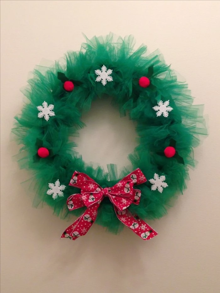 forest green tulle, shaped into a christmas wreath, decorated with white snowflake ornaments, wreath ideas, red pattrened bow, and red holly berries, with green leaves, made from felt