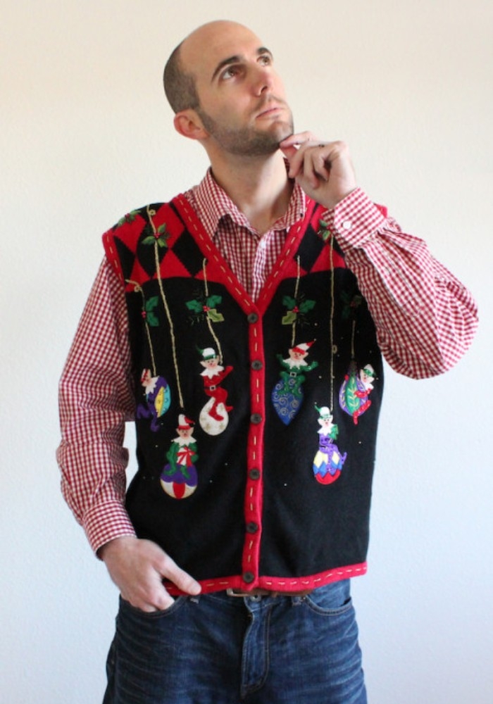 toughtful man in a checkered, red and white shirt, and blue jeans, wearing a black and red vest, decorated with elves, and baubles in different colors