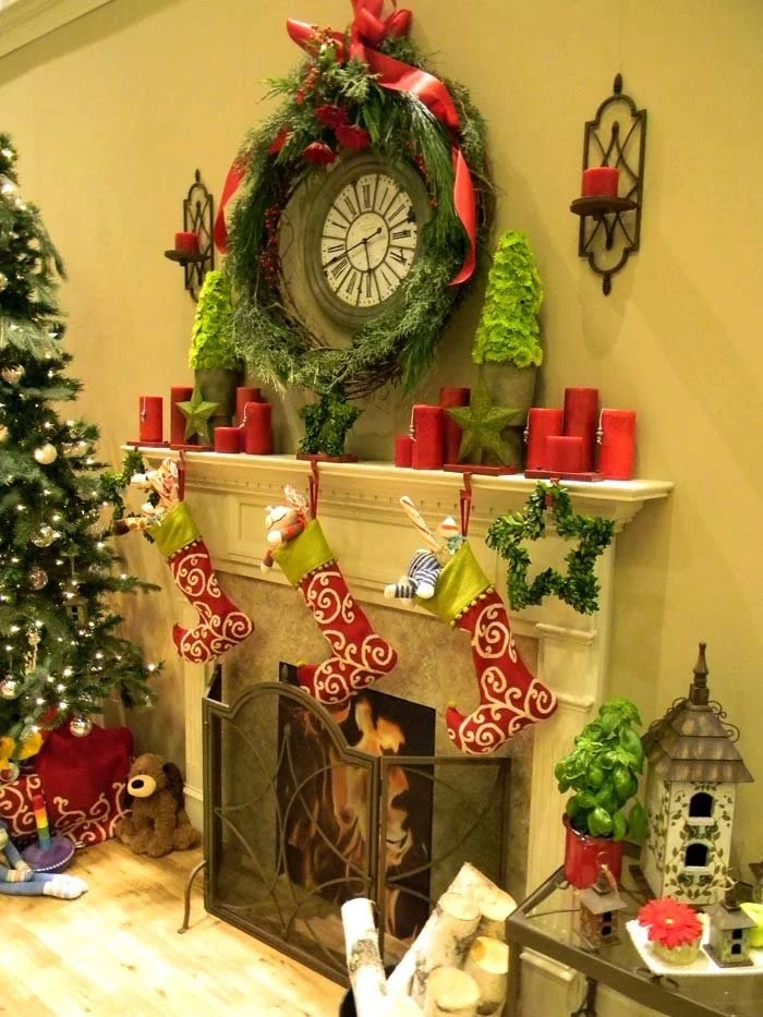 round old-looking clock, surrounded by a green pine garland, and red candles, images of christmas, above a fireplace, with three red, white and lime green stockings