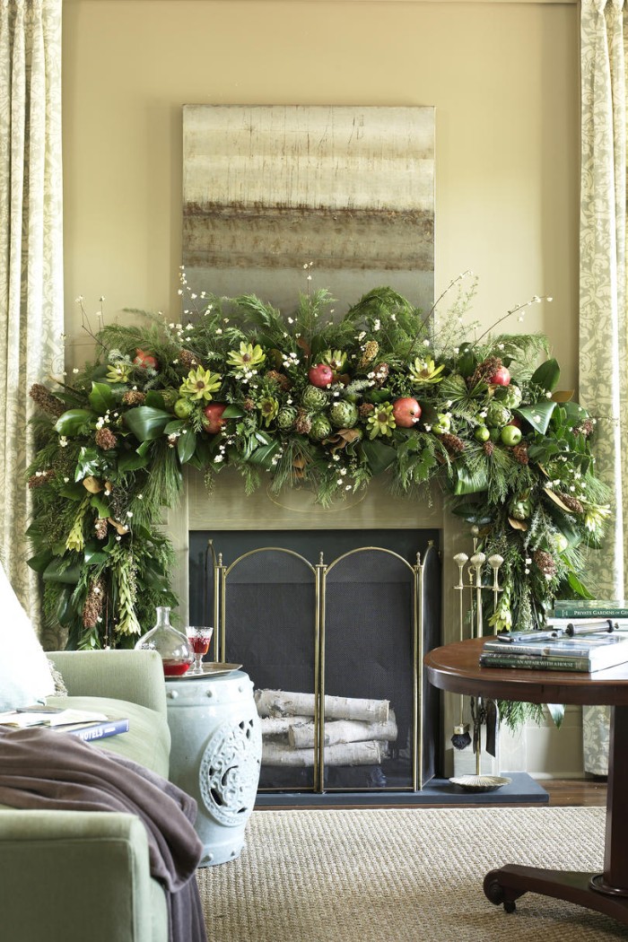 yellow flowers and red pomegranates, green apples and various leaves, on a lush green garland, decorating a diy fireplace mantel, in a room with beige walls