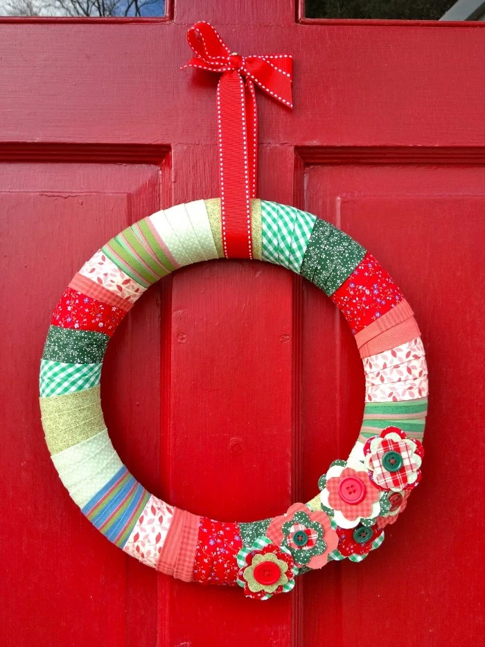 simple wreath made from a hoop, covered with patterned, and plain washi tape, in different colors, and decorated with colorful paper flowers and buttons, christmas wreath ideas, on a red door