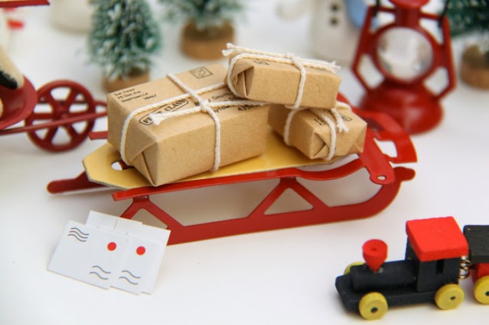 red sleigh figurine, with three small presents, wrapped in beige paper, and tied with white string, three tiny letters, and other toys, advent calendar filling