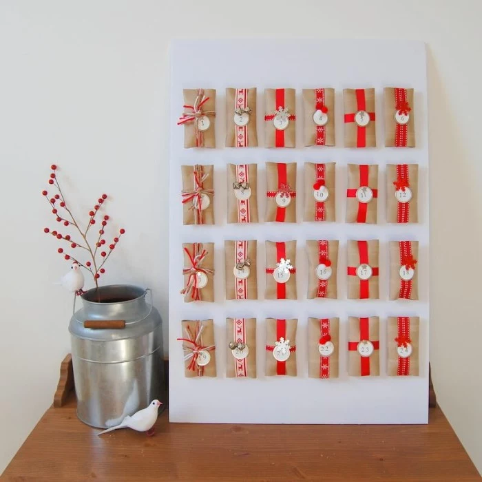 twenty four small gifts, wrapped in beige paper, and decorated with red patterned, and plain ribbons, and round numbered labels, attached to a rectangular white board, advent calendar ideas